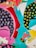 An abstract composition featuring vibrant colors and bold shapes. Circular patterns in blue on dark backgrounds and yellow spots on another section. Triangular white shapes and flowing brushstrokes intermingle with red, pink, and turquoise accents.