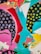 An abstract composition featuring vibrant colors and bold shapes. Circular patterns in blue on dark backgrounds and yellow spots on another section. Triangular white shapes and flowing brushstrokes intermingle with red, pink, and turquoise accents.