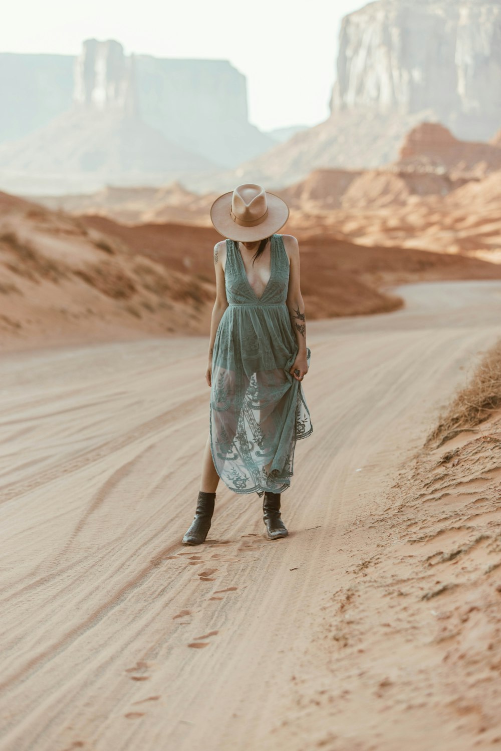 woman in green tank top and blue skirt walking on brown sand during daytime