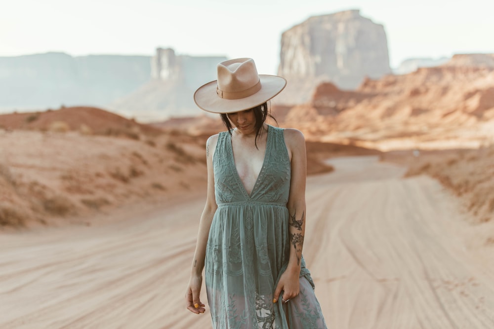 woman in blue sleeveless dress wearing white cowboy hat walking on brown sand during daytime