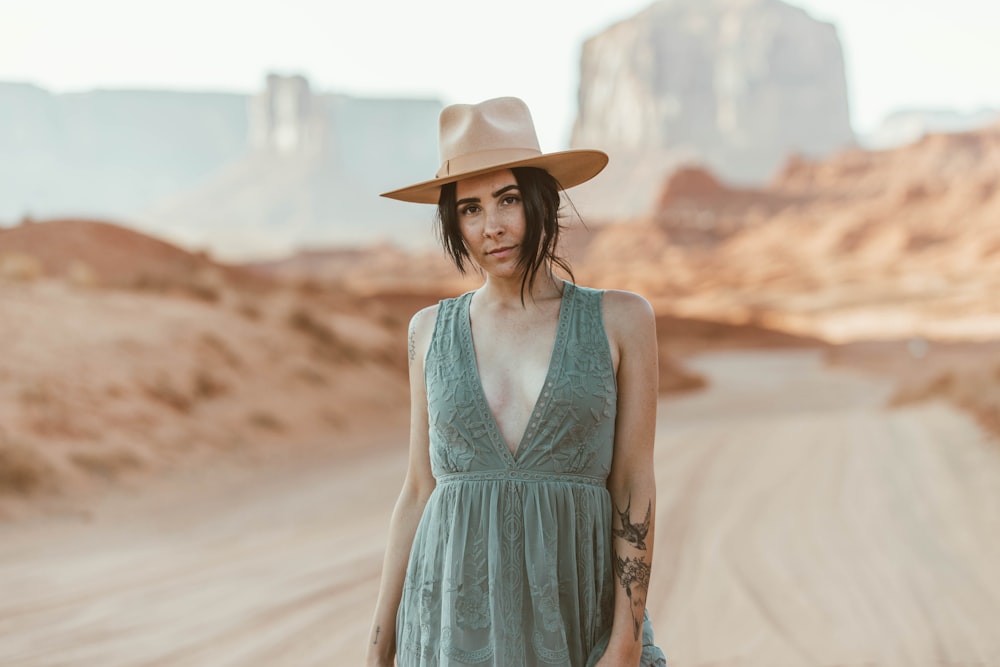 woman in blue sleeveless dress wearing brown hat standing on brown sand during daytime