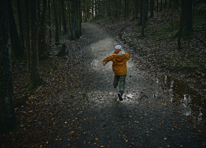 child in brown jacket walking on pathway