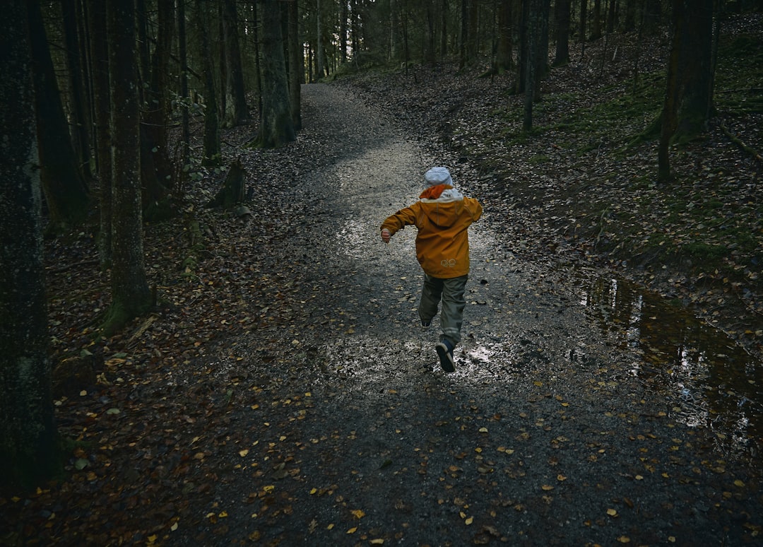 child in brown jacket walking on pathway