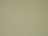 A close-up of a textured wall surface with a rough, uneven finish displaying numerous small bumps and grains.