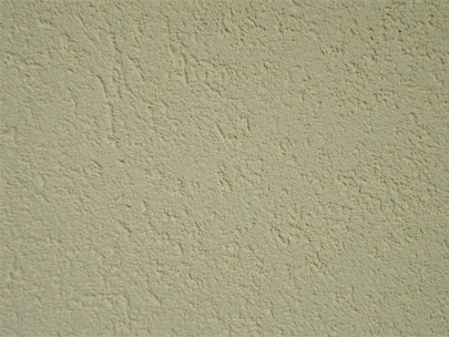 A close-up of a textured wall surface with a rough, uneven finish displaying numerous small bumps and grains.