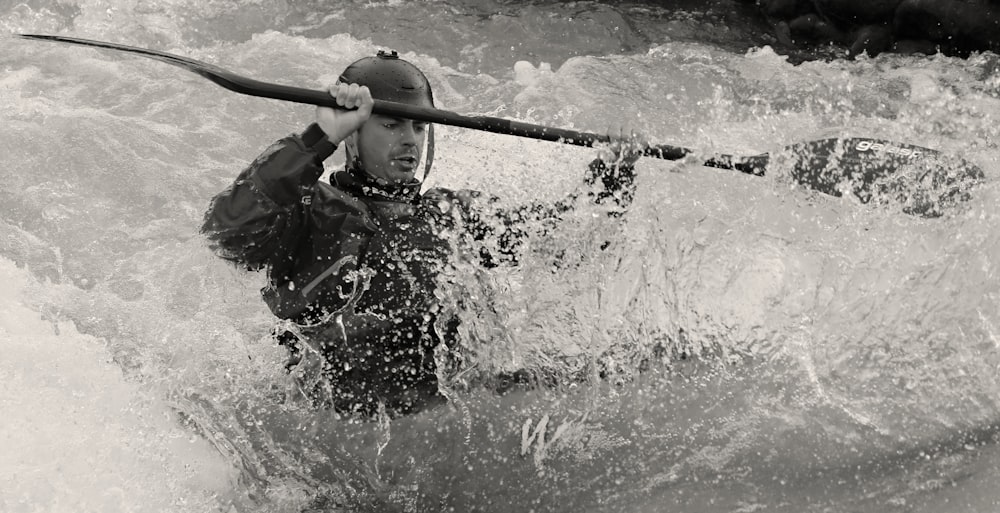 man in black jacket holding a stick in water