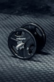 Close-up of a sleek, black dumbbell with textured grip resting on a gym floor.