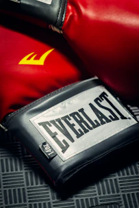 Close-up of high-quality boxing gloves and shin guards arranged on a sleek dark surface under stadium lights.