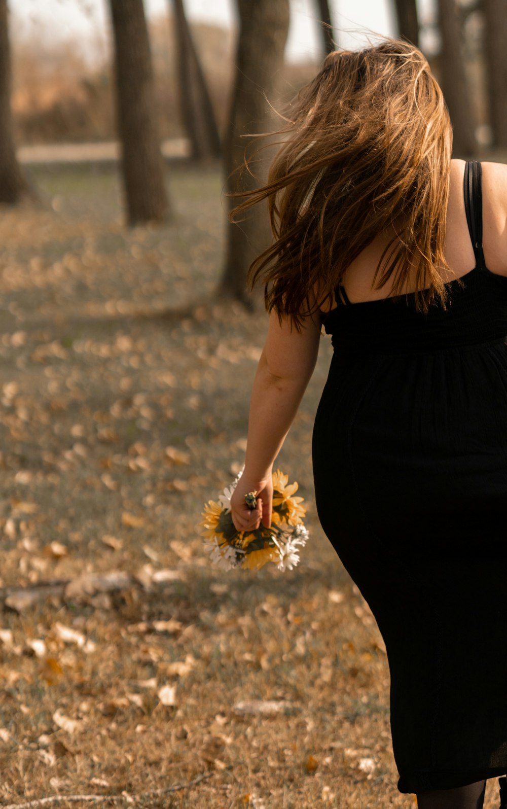 Frau in schwarzem Kleid mit braunen getrockneten Blättern