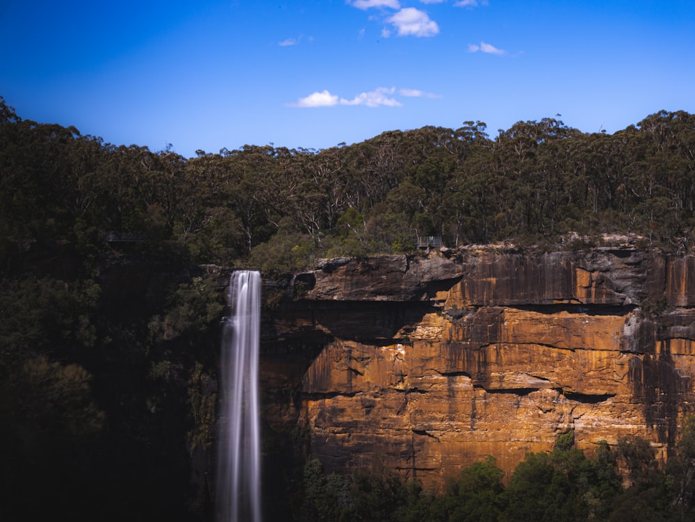 waterfalls on brown rocky mountain under blue sky during daytime