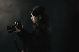 A candid portrait of Drew Franks holding a camera against a dark, moody background.