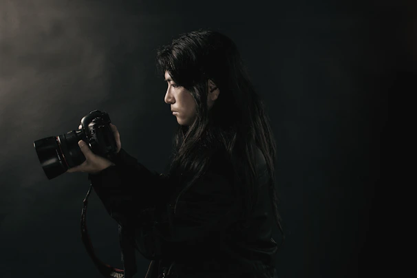 A candid portrait of Drew Franks holding a camera against a dark, moody background.