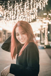 A warm photo of a woman smiling against a backdrop of colorful city lights at dusk in Taiwan.