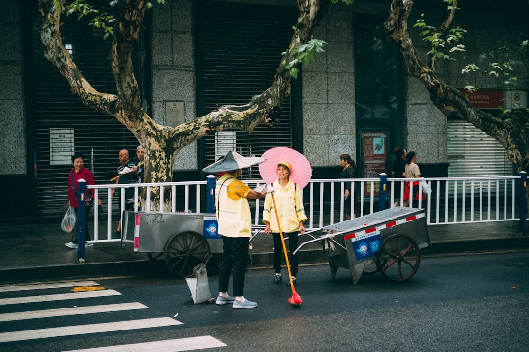 woman in yellow long sleeve shirt and gray pants holding pink umbrella walking on sidewalk during