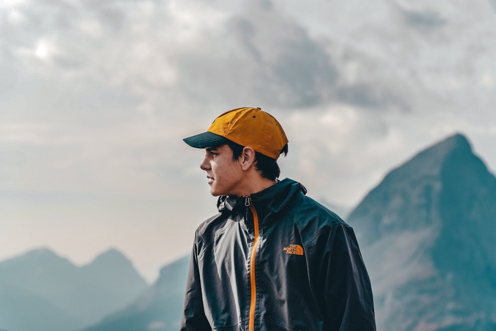昼間、山に立つ青いジャケットと黄色い帽子をかぶった男