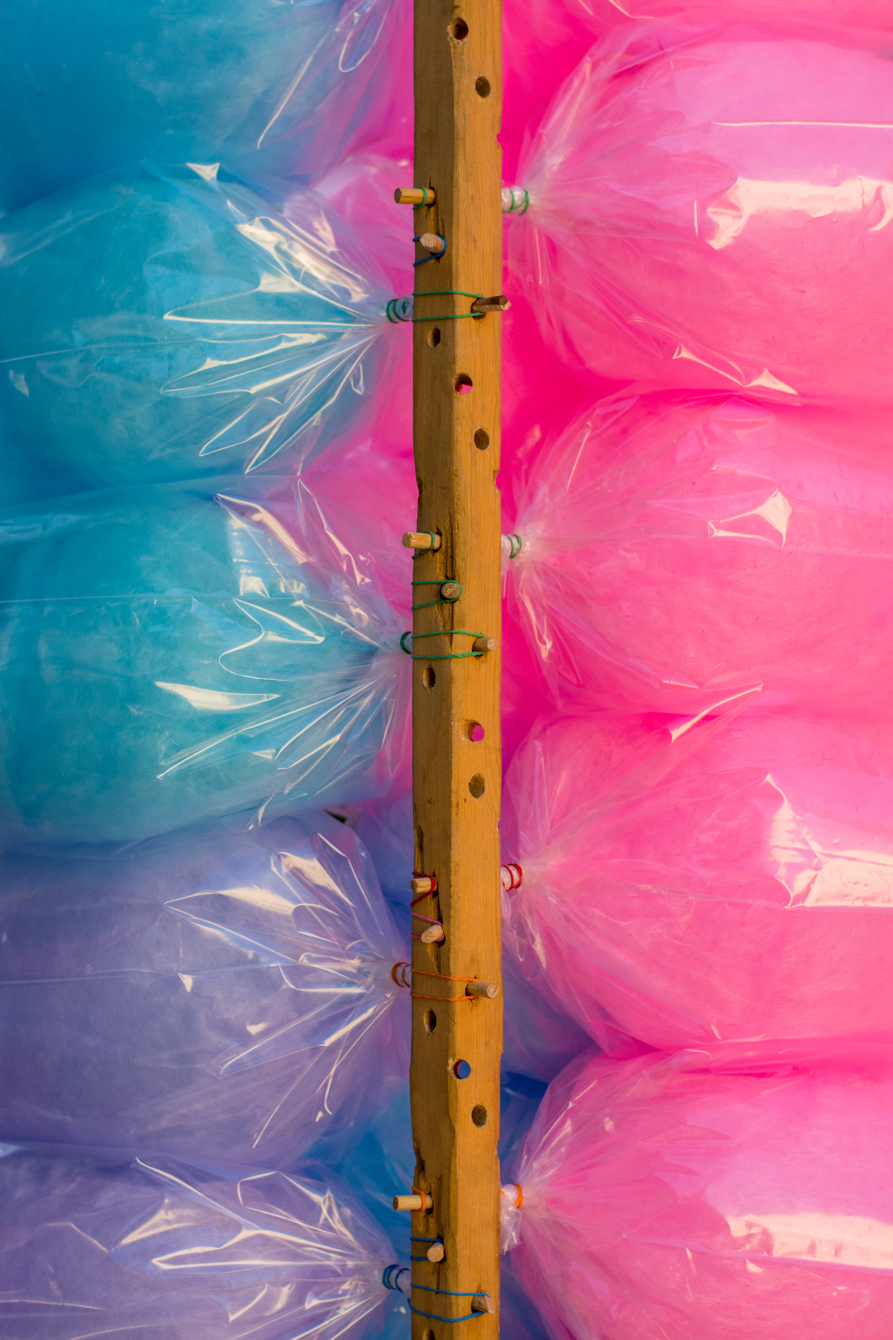 Clear bags of blue and pink cotton candy tied in rows to a wooden pole