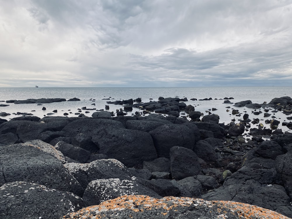 black and gray rocks on seashore under white clouds during daytime