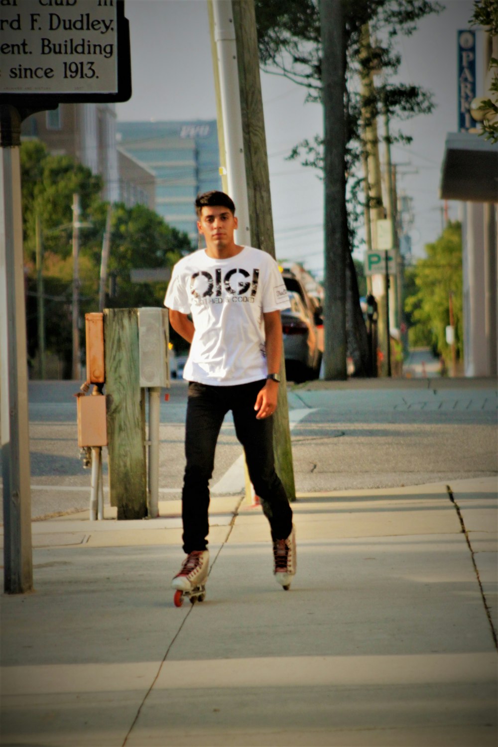 man in white crew neck t-shirt and black pants standing on sidewalk during daytime