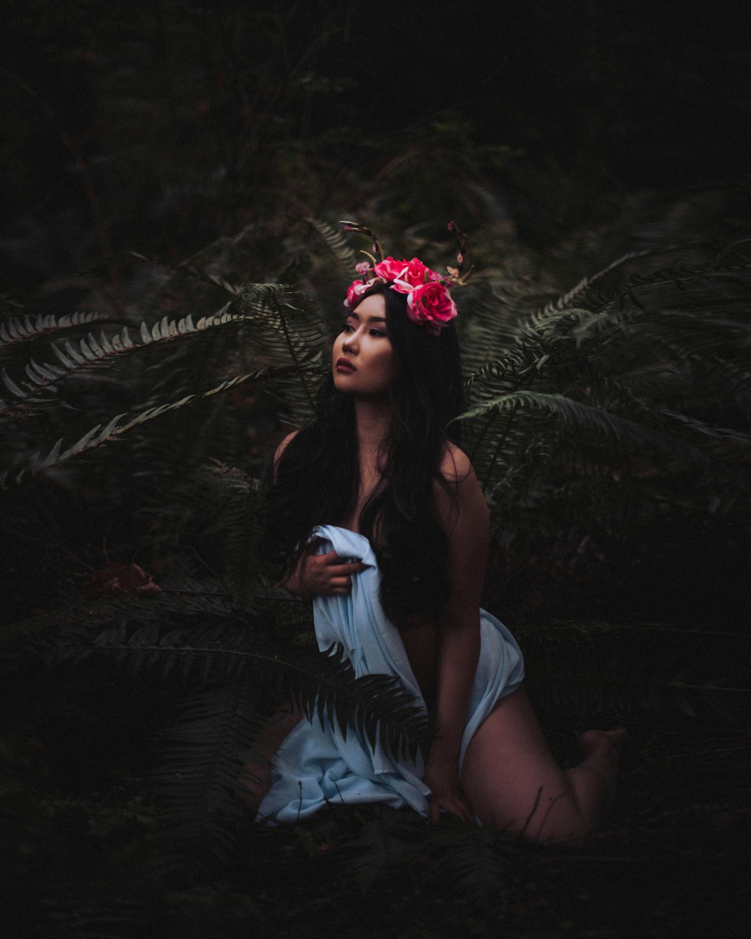 woman in white long sleeve shirt sitting on ground surrounded by green plants