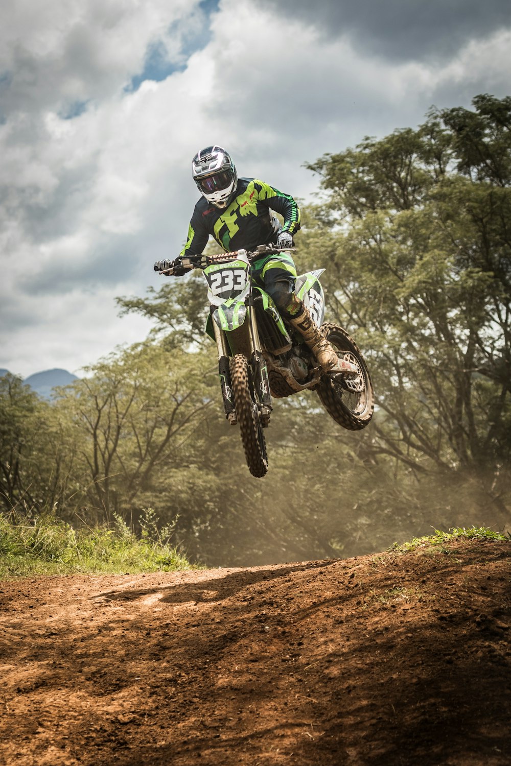 homem no capacete verde e branco do motocross que monta a bicicleta da sujeira do motocross