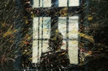 A window is seen with a reflection that appears to be partially obscured by various streaks and splatters of paint. The colors are scattered across the surface, creating an abstract and dynamic visual pattern.