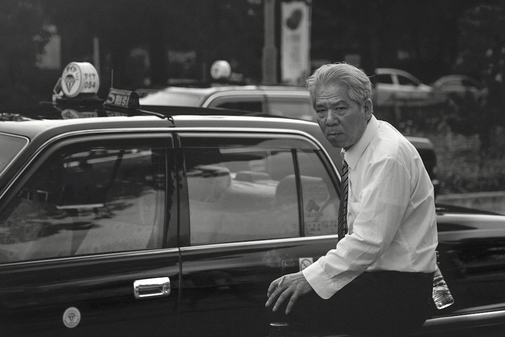 man in white dress shirt leaning on black car