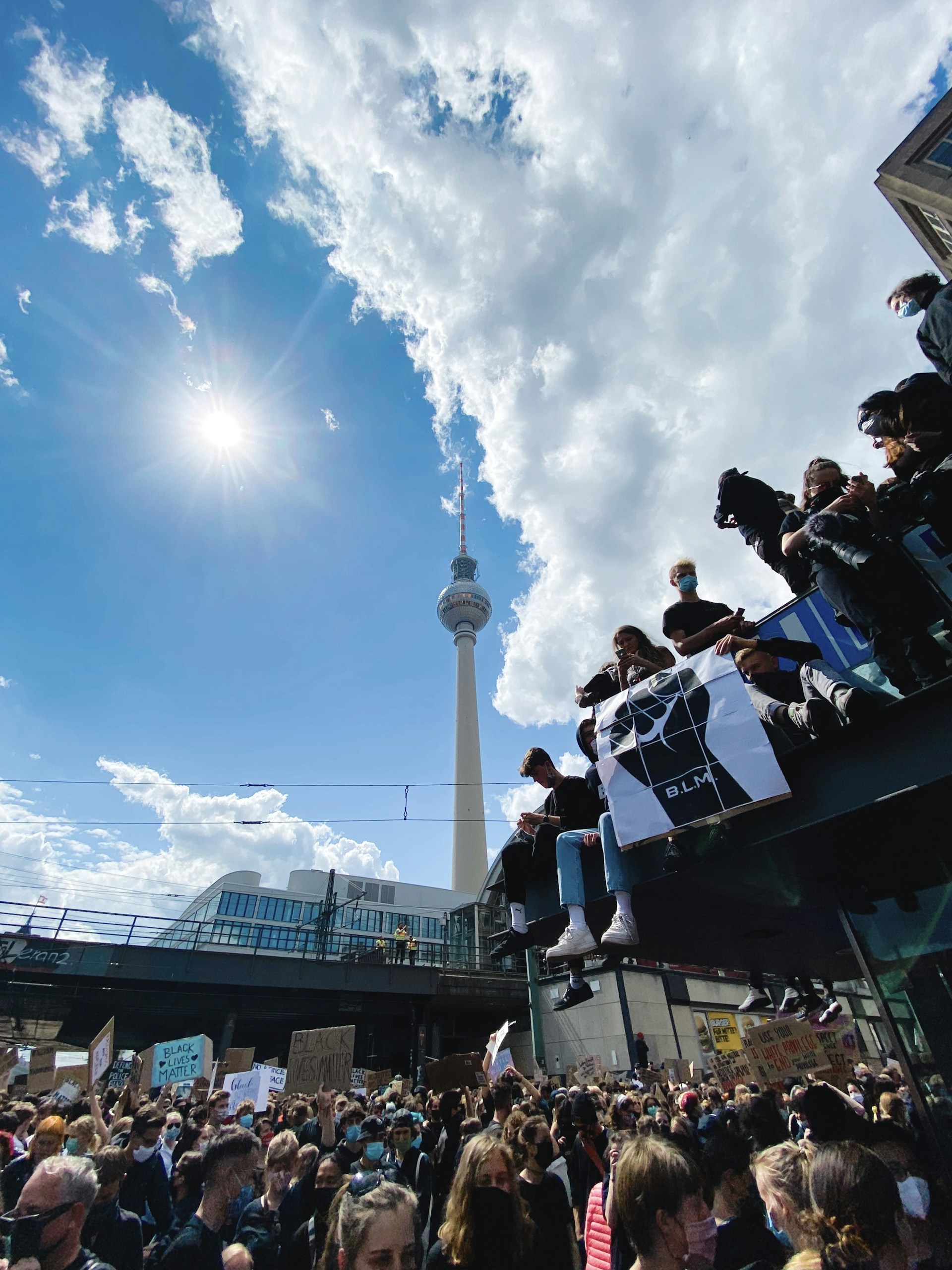 A dynamic scene from a local protest, showing a crowd of passionate people holding signs and banners, with the city skyline blurred in the background.