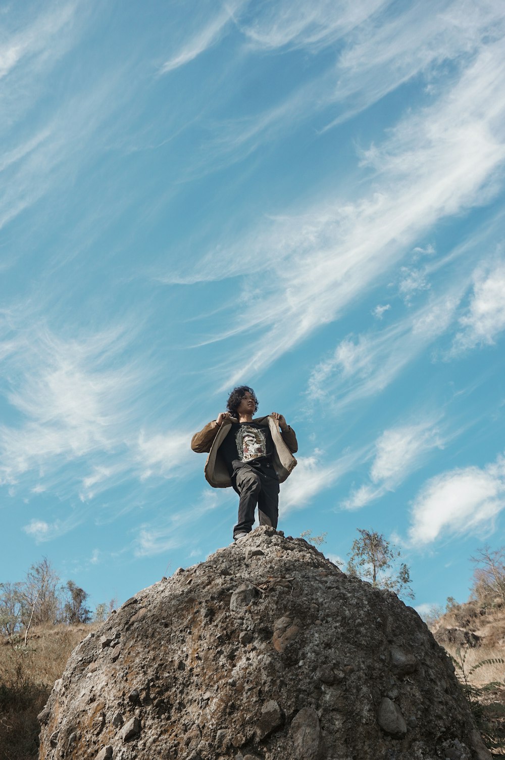 man in black jacket sitting on rock under blue sky during daytime