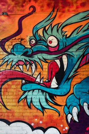 A vibrant mural of a dragon with exaggerated features including large eyes, sharp teeth, and a swirling, elongated tongue. The dragon is set against a fiery orange and red background, creating a striking contrast with its blue and teal scales.