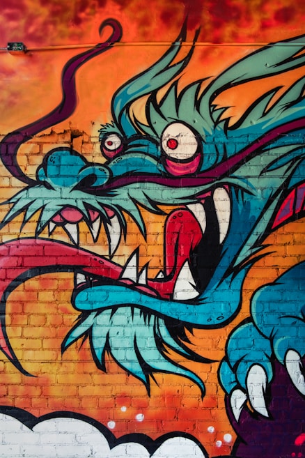 A vibrant mural of a dragon with exaggerated features including large eyes, sharp teeth, and a swirling, elongated tongue. The dragon is set against a fiery orange and red background, creating a striking contrast with its blue and teal scales.