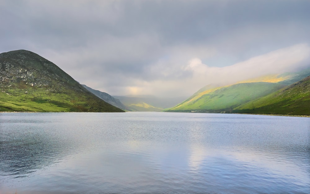 green mountains beside body of water under white sky during daytime