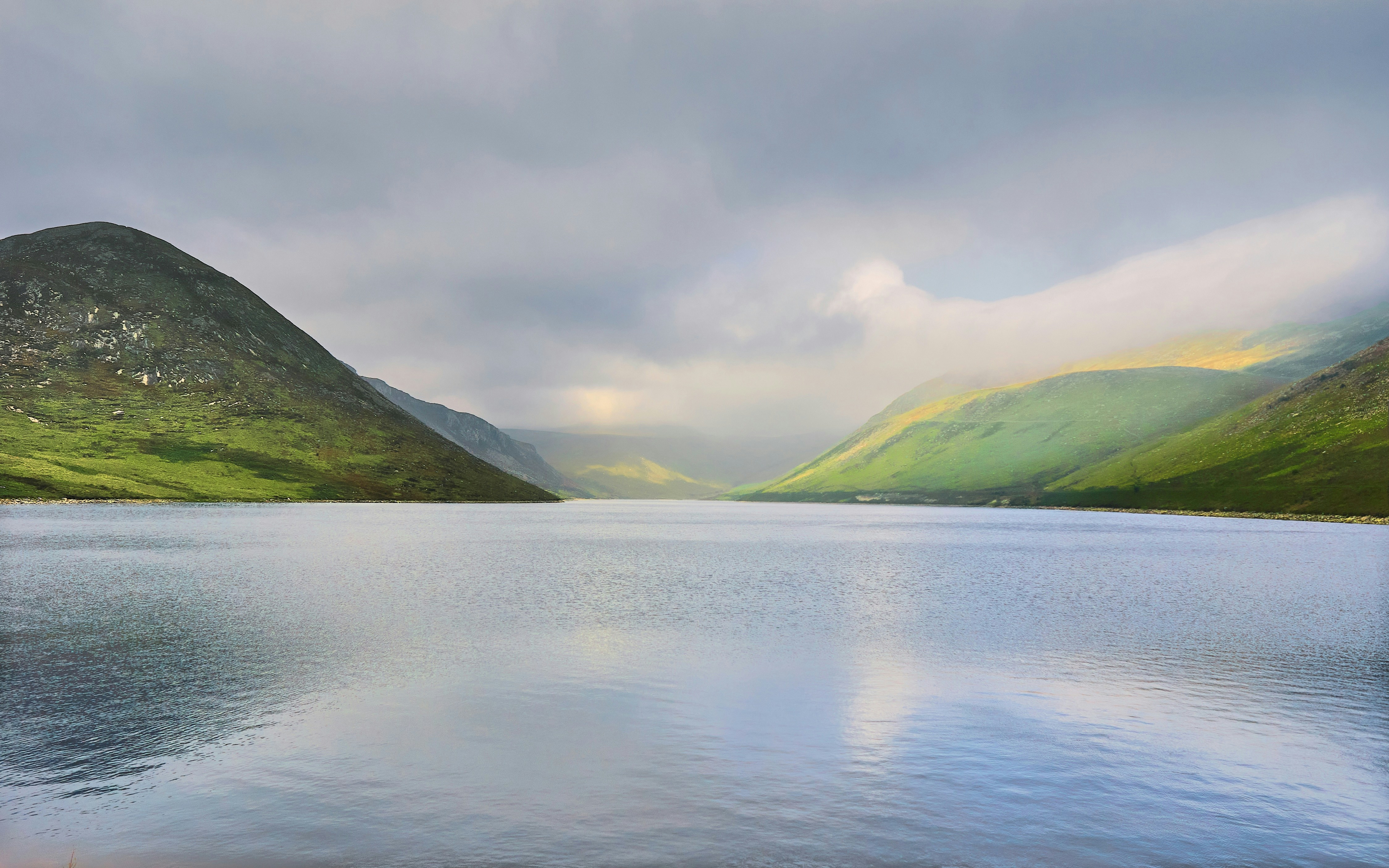 green mountains beside body of water under white sky during daytime