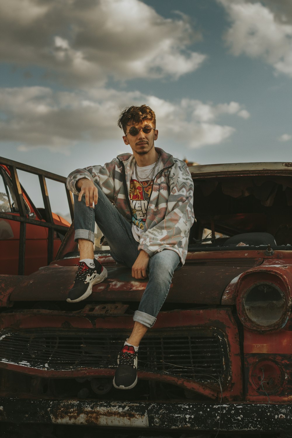 homem na camisa social floral branca e vermelha e jeans azul sentado no carro vermelho