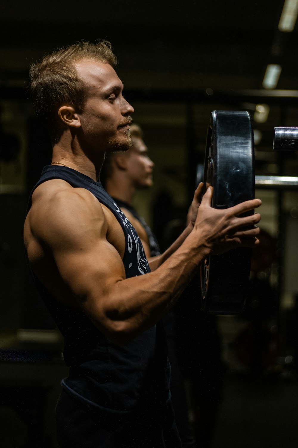 man in black tank top holding black smartphone