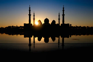 A serene mosque silhouette at sunset with soft green and gold accents reflecting peace and spirituality.