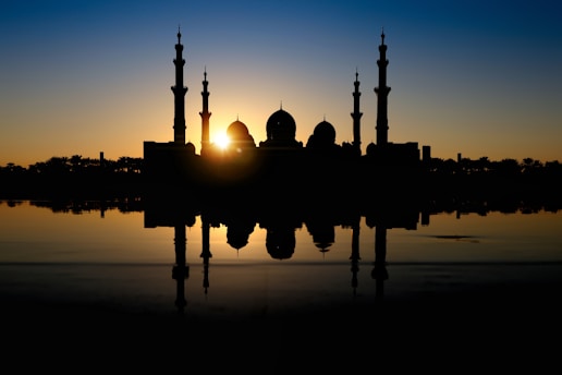 A serene mosque silhouette at sunset with emerald and gold accents reflecting the website's color theme.