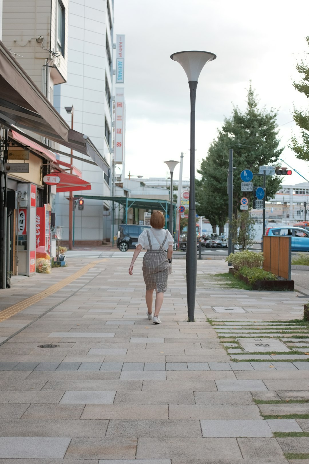 woman in blue and white plaid dress shirt walking on sidewalk during daytime