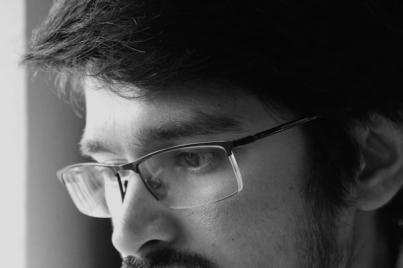 Young South Asian man looking sad and frustrated, grayscale portrait by a window