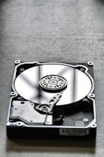 A close-up view of an open hard disk drive, showing its reflective platter and read/write arm. The disk is placed on a textured surface, creating a contrasting background.