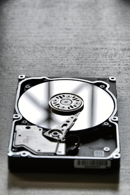 A close-up view of an open hard disk drive, showing its reflective platter and read/write arm. The disk is placed on a textured surface, creating a contrasting background.