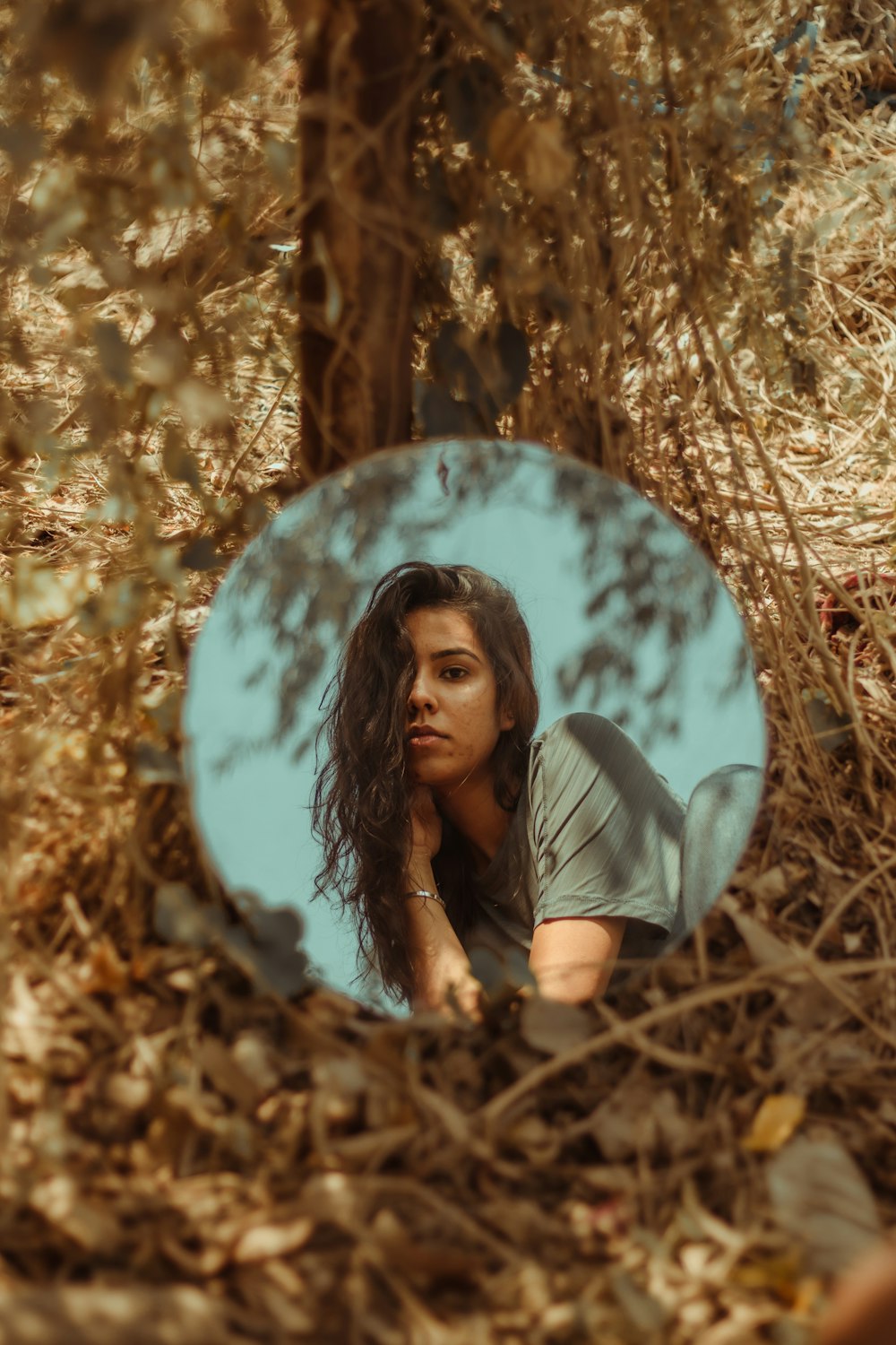 woman in gray t-shirt sitting on brown dried leaves during daytime