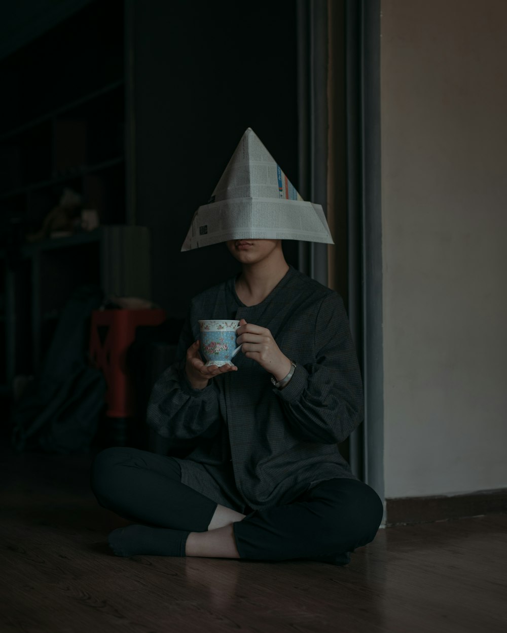 man in black jacket and black pants sitting on floor while holding white ceramic mug