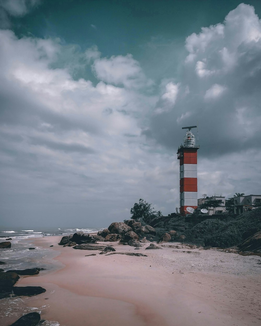 red and white lighthouse on brown sand near body of water during daytime