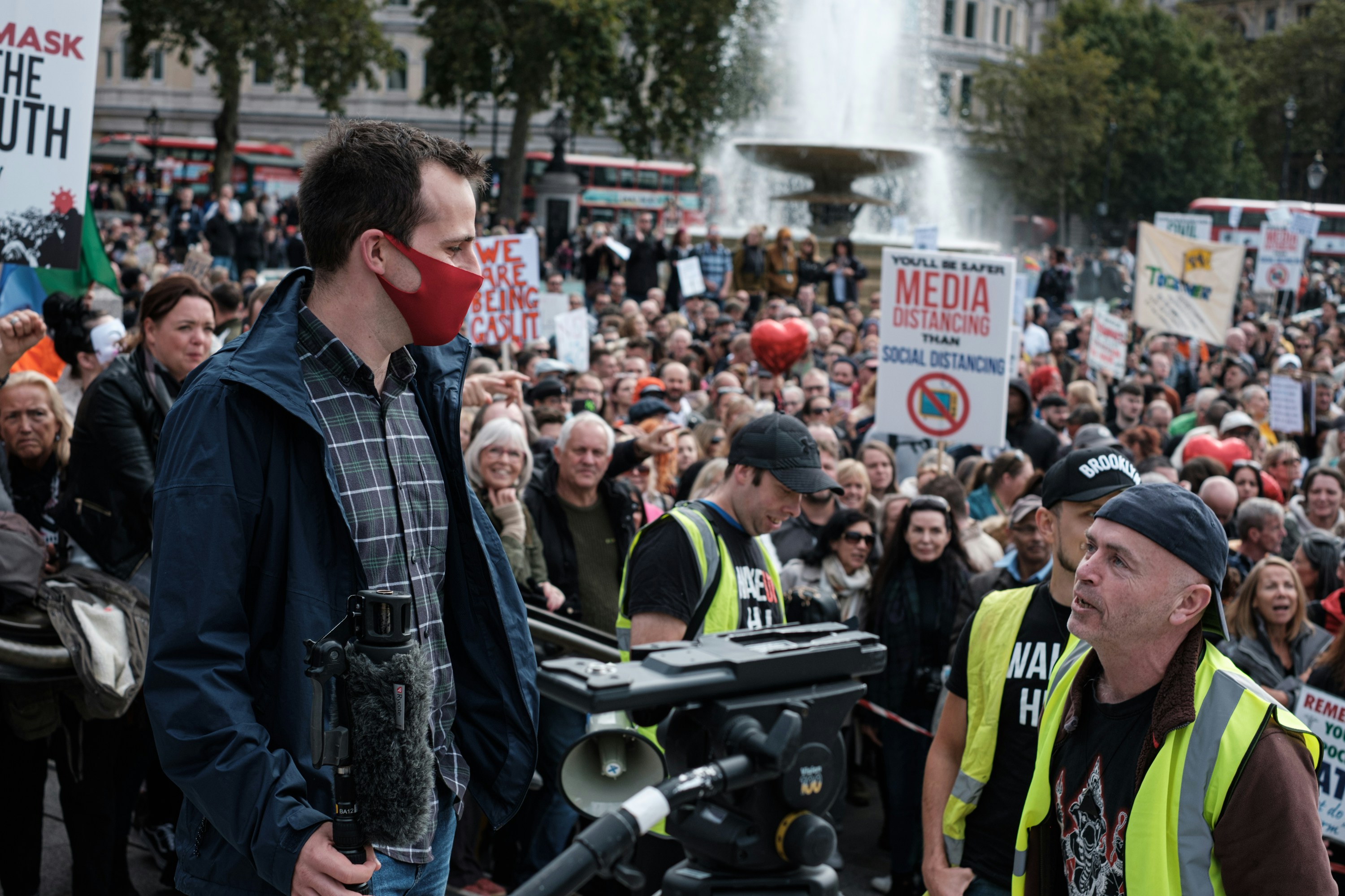Man with microphone records protest in urban square.