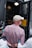 A person wearing a white cap and a checkered shirt is handcuffed and being escorted by police officers. The scene appears to be outside, near a police van with an open door, suggesting an arrest is taking place.