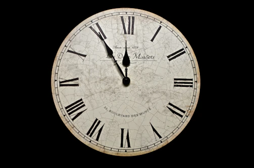 A vintage clock with its hands spinning backward against a dark background.