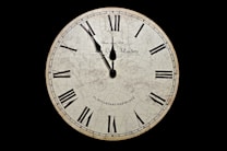 A vintage clock with Roman numerals is set against a dark background. The clock face has an aged appearance, featuring crack patterns and subtle staining. The hands of the clock are positioned at ten minutes past ten.