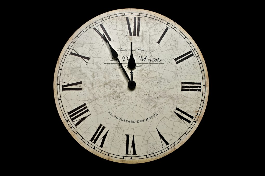Horloge ancienne à chiffres romains et cadran craquelé, les aiguilles proches de midi, sur fond noir