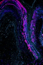 Swirling patterns of vibrant magenta and deep purple flow through a predominantly black backdrop, creating an abstract and cosmic aesthetic. Specks of white resemble stars scattered across a night sky, enhancing the ethereal feel.