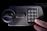 A hand presses the number 0 on an electronic keypad. The keypad is attached to a grey safe with a round handle and the words EASY HOME written above the keypad.